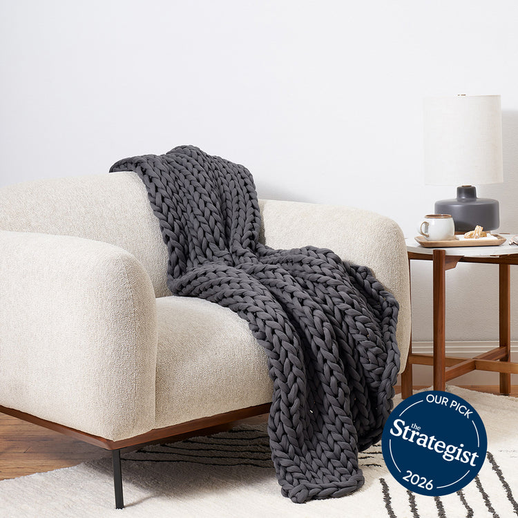 Bearaby Grey knitted blanket draped over a beige armchair in a living room setting with 'The Strategist' 2026 badge.