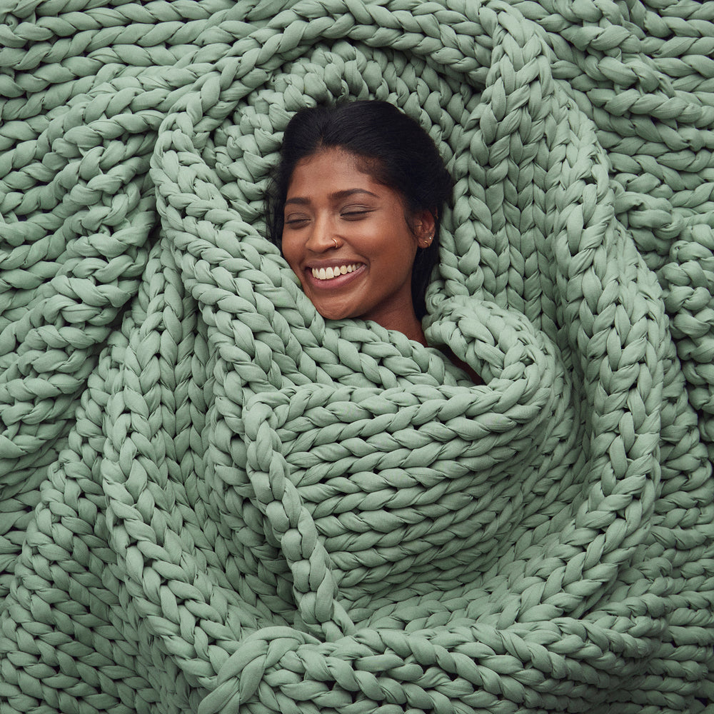 Woman smiling and wrapped in a botanical dream knitted blanket