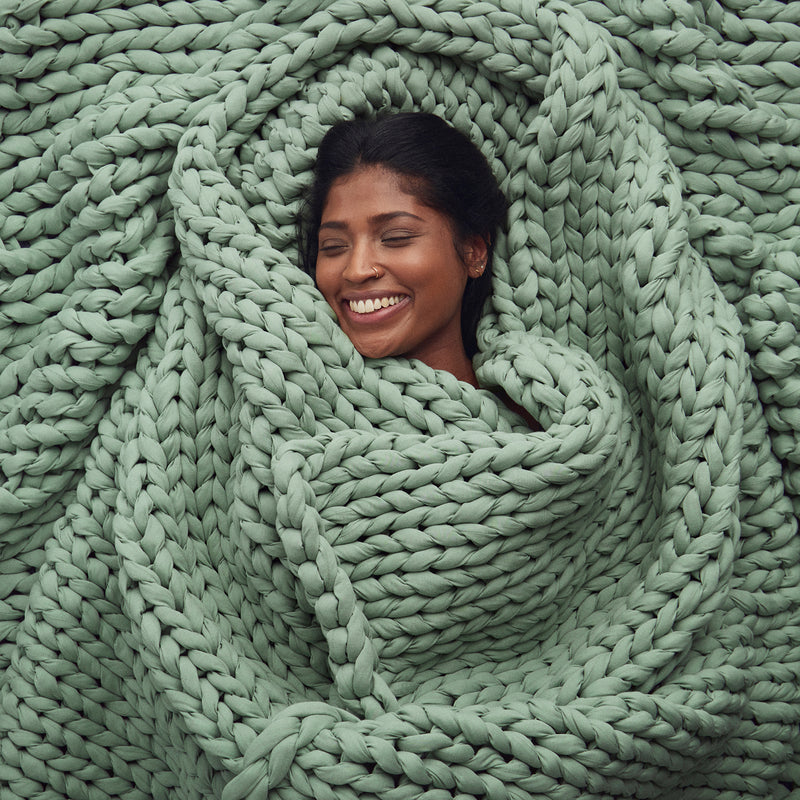 Woman smiling and wrapped in a botanical dream knitted blanket