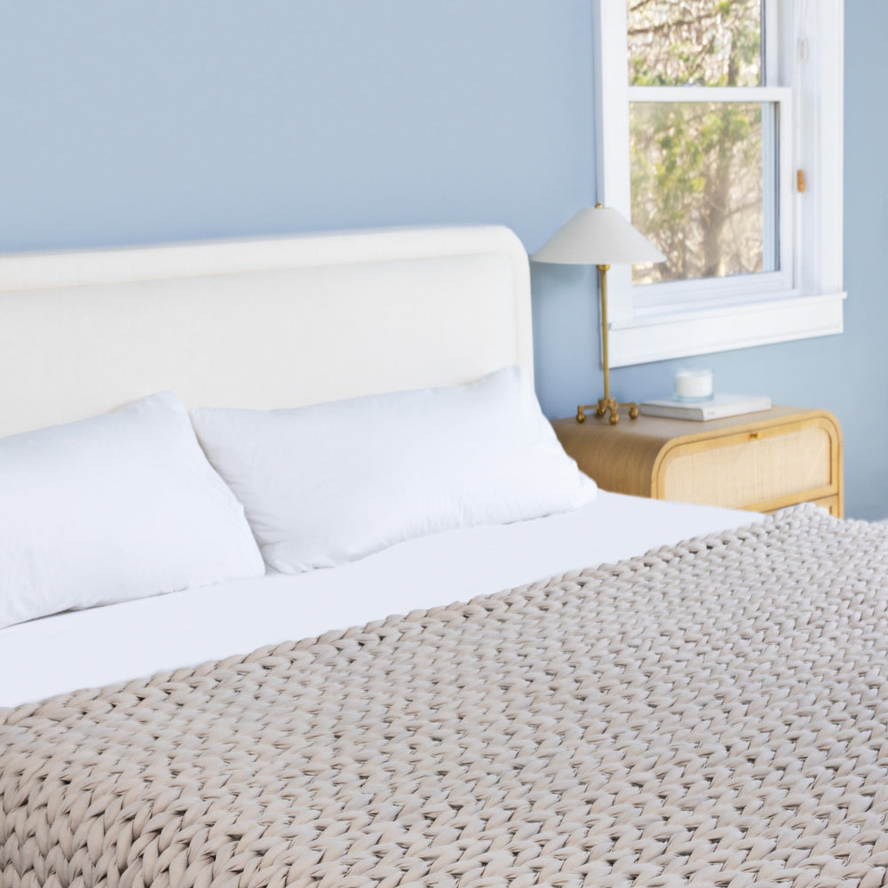 Neatly made bed with white bedding and a textured driftwood ocean napper