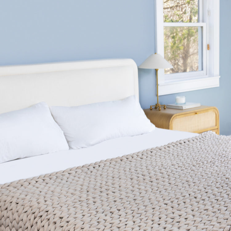 Neatly made bed with white bedding and a textured driftwood ocean napper