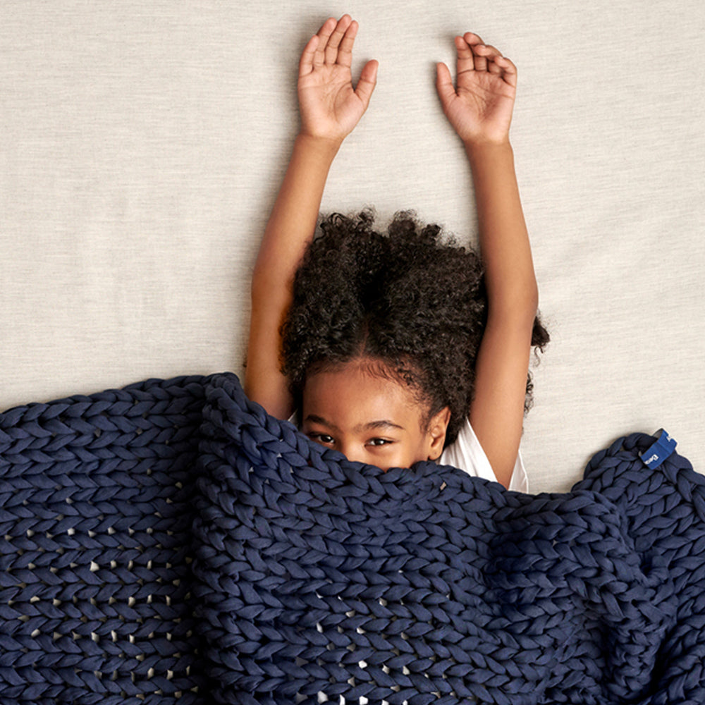 Child covered by a midnight blue kids knitted blanket with arms raised