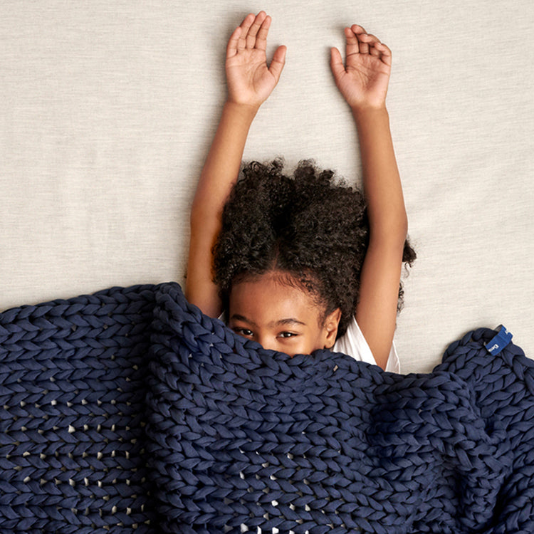 Child covered by a midnight blue kids knitted blanket with arms raised