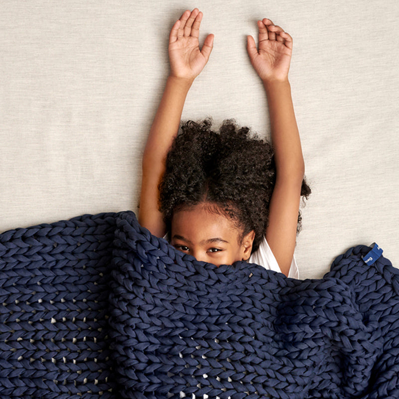 Child covered by a midnight blue kids knitted blanket with arms raised