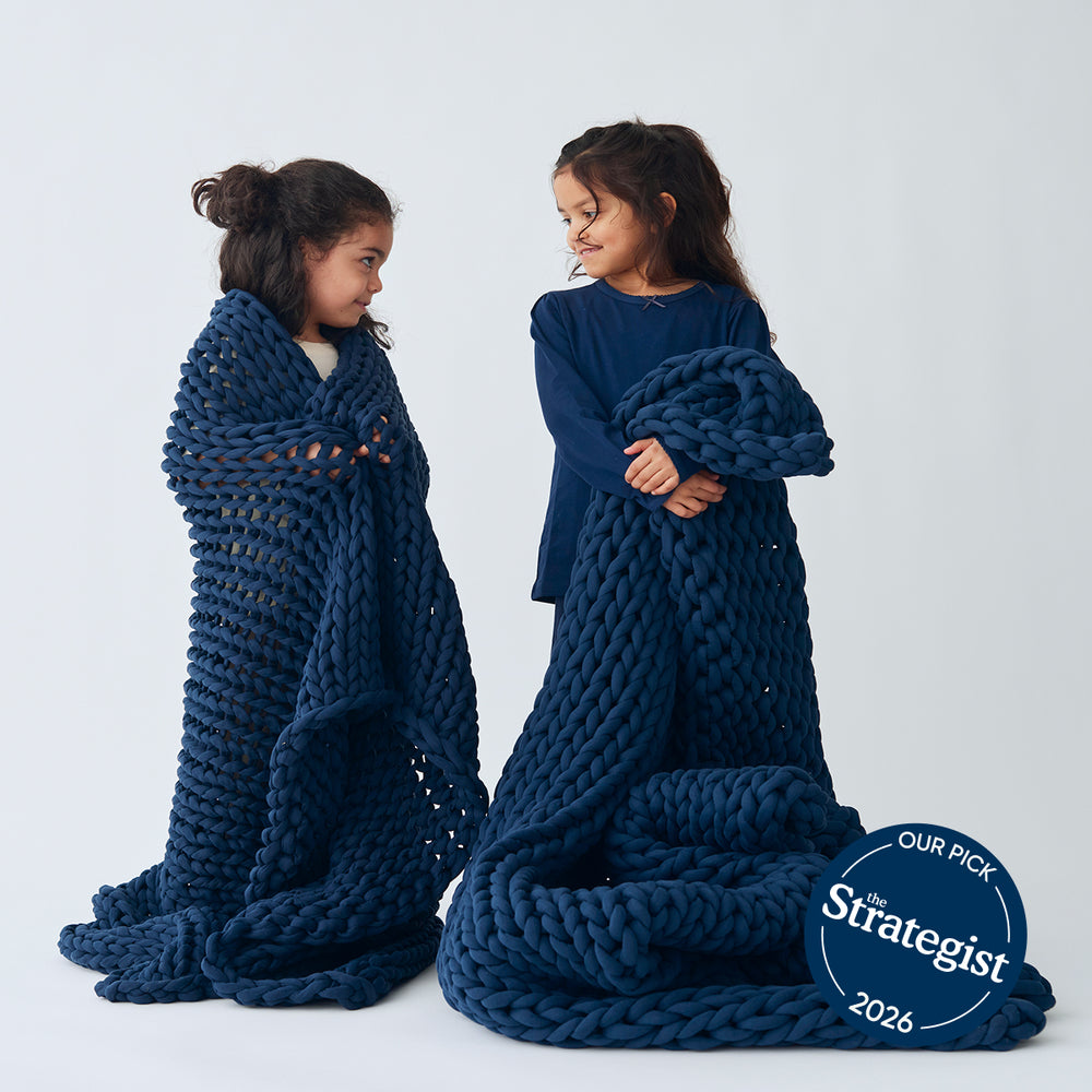 Two children wrapped in a large midnight blue knitted blanket on a white background, with 'The Strategist' 2026 badge.