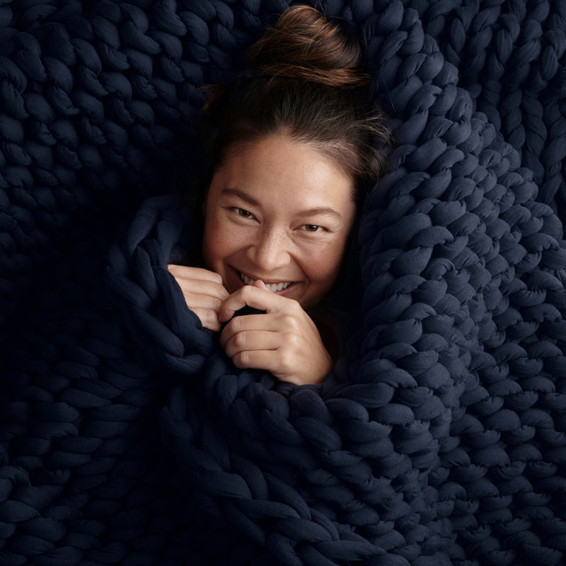 Person wrapped in a midnight blue bearaby weighted blanket, smiling.