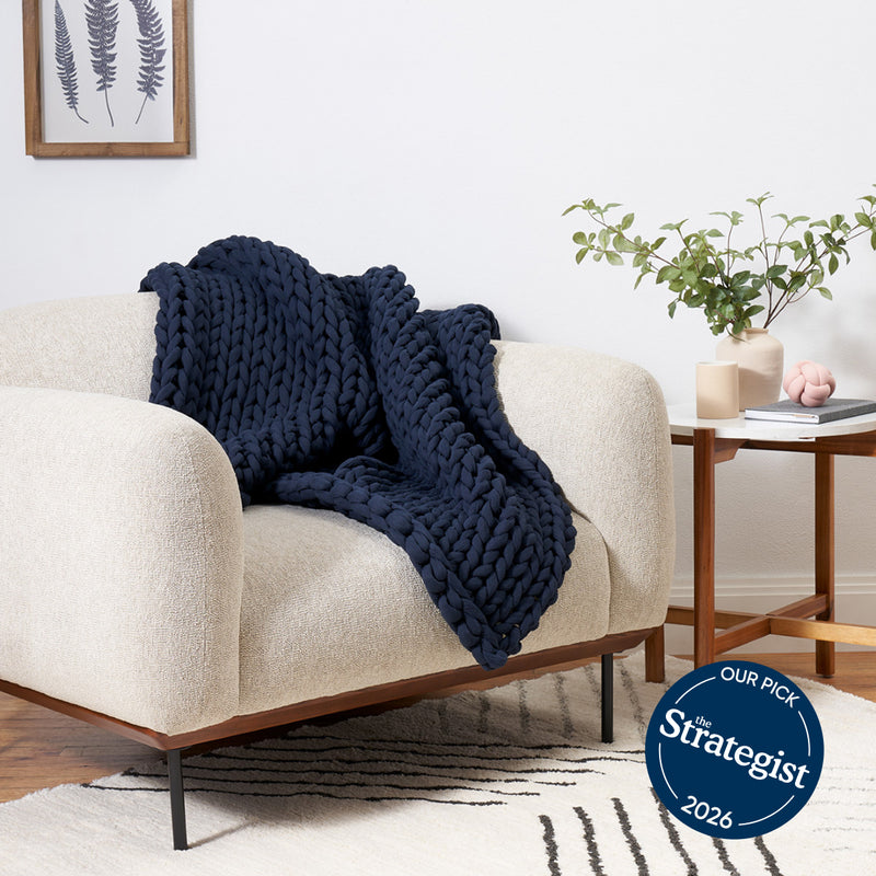 bearaby Navy blue chunky knit blanket draped over a beige sofa in a living room setting.