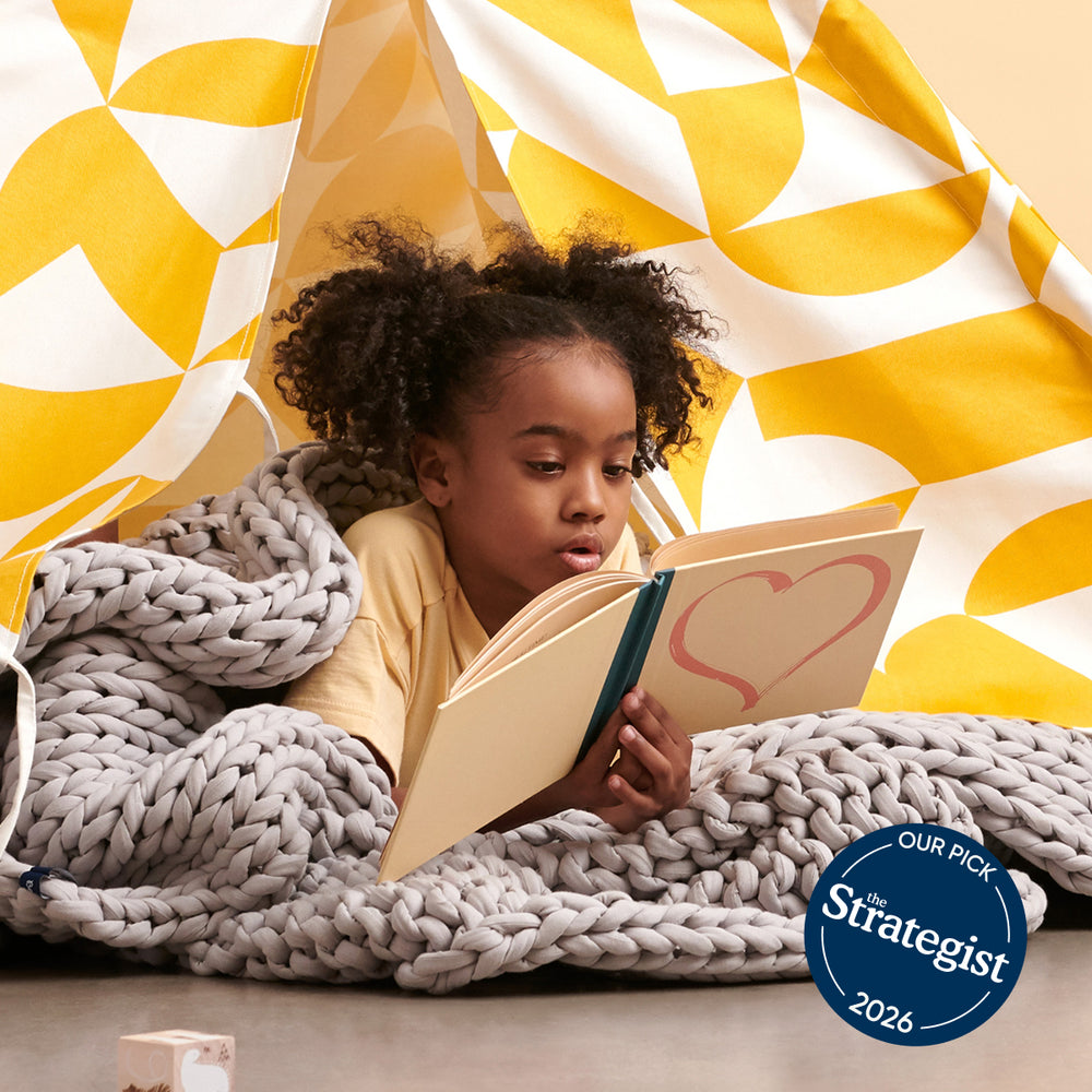 Child reading a book with a moonstone grey kids weighted blanket with a 'The Strategist' 2026 badge.