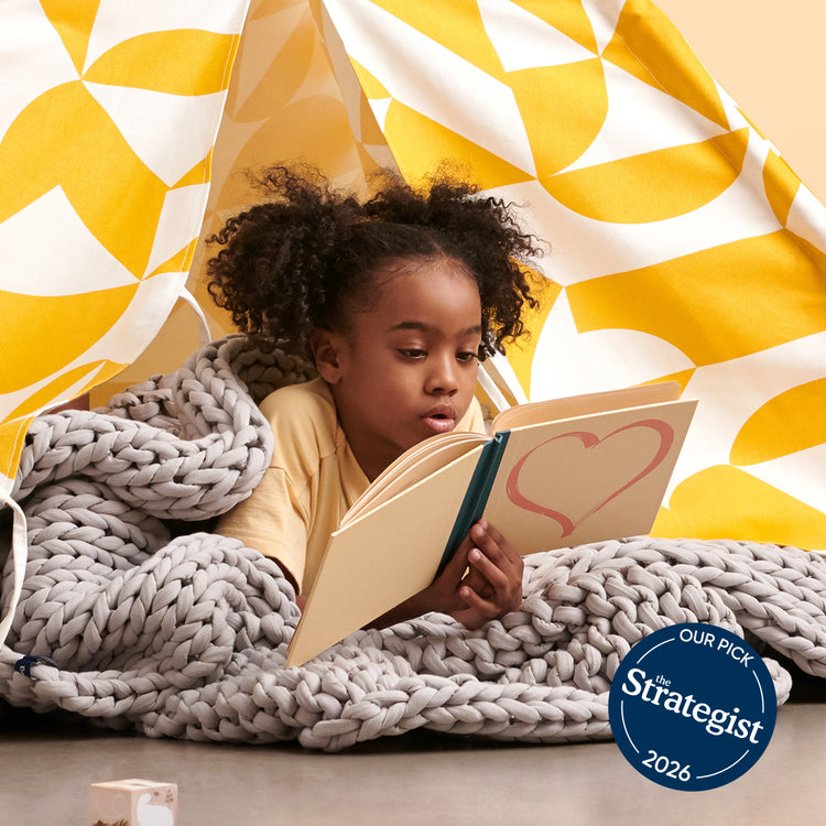 Child reading a book with a moonstone grey kids weighted blanket with a 'The Strategist' 2026 badge.