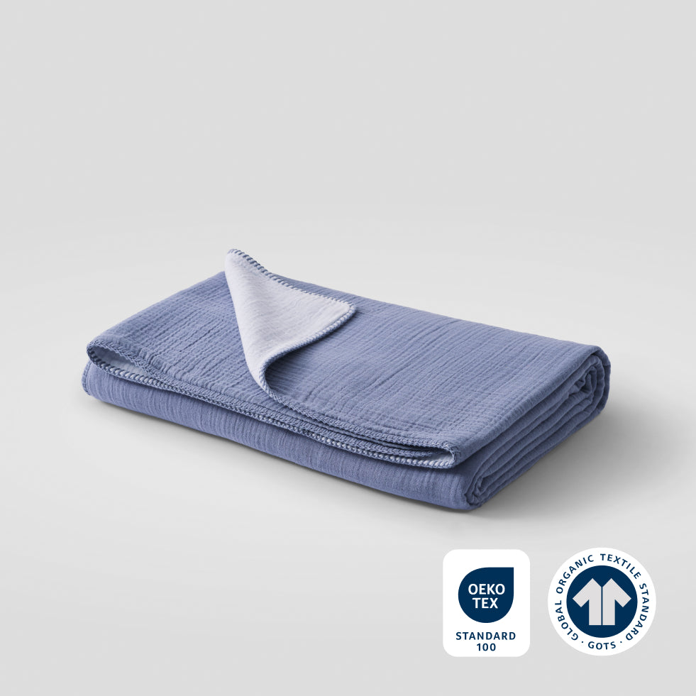 A folded ocean whisper cotton muslin blanket with OEKO-TEX and GOTS certification badges in the lower right corner
