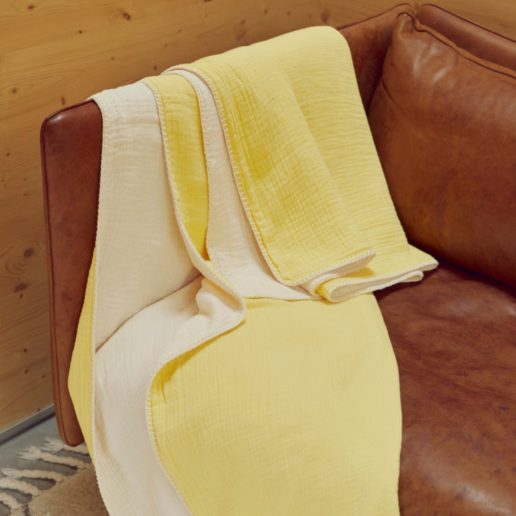 A folded lemon blanket throw blanket over a brown leather couch
