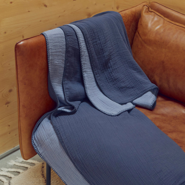 A folded midnight blue throw blanket over a brown leather couch