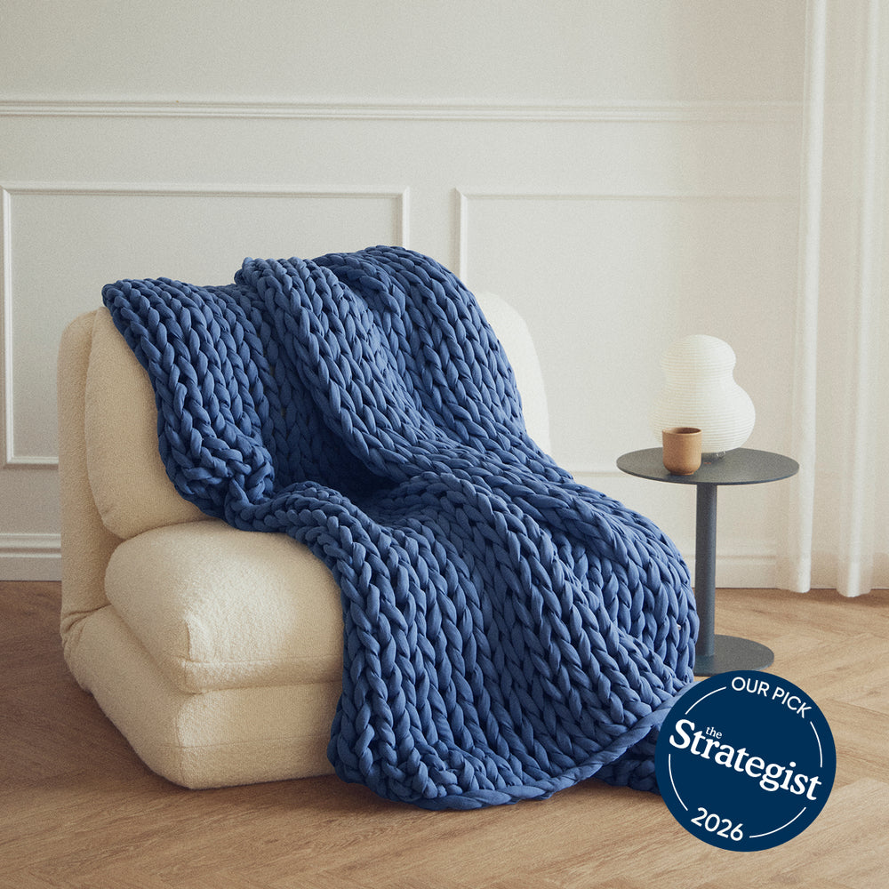 Ocean Blue knitted blanket draped over a beige armchair in a room with a side table and decorative items.