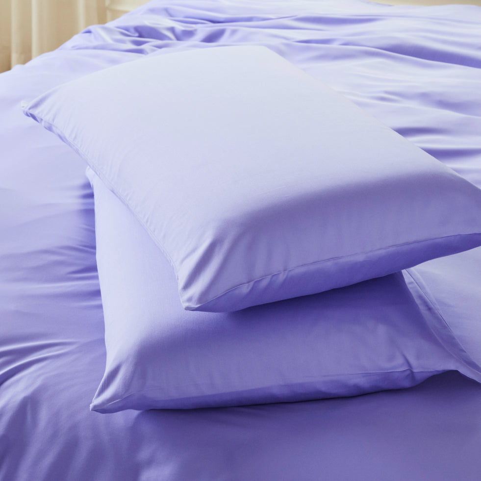 Two lavender-colored bearaby pillowcase stacked on top of matching lavender bedding