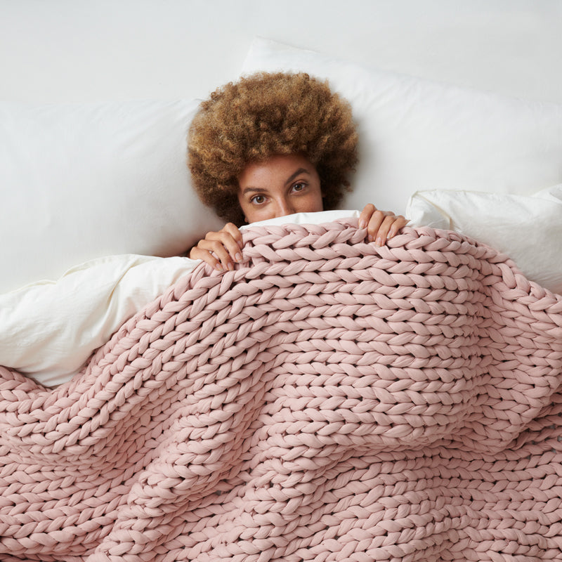 Lady tugging in under a hand knit weighted blanket without glass beads covering the duvet